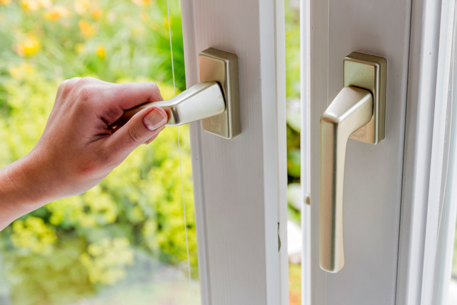 Frau öffnet ein Fenster zum Lüften. Zu sehen ist nur die Hand und das Fenster in nahaufnahme.