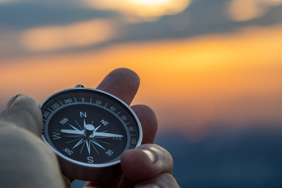 Ein Kompass in einer Hand mit einem schönen Sonnenuntergang im Hintergrund - Symbolbild für die richtige Richtung einschlagen.