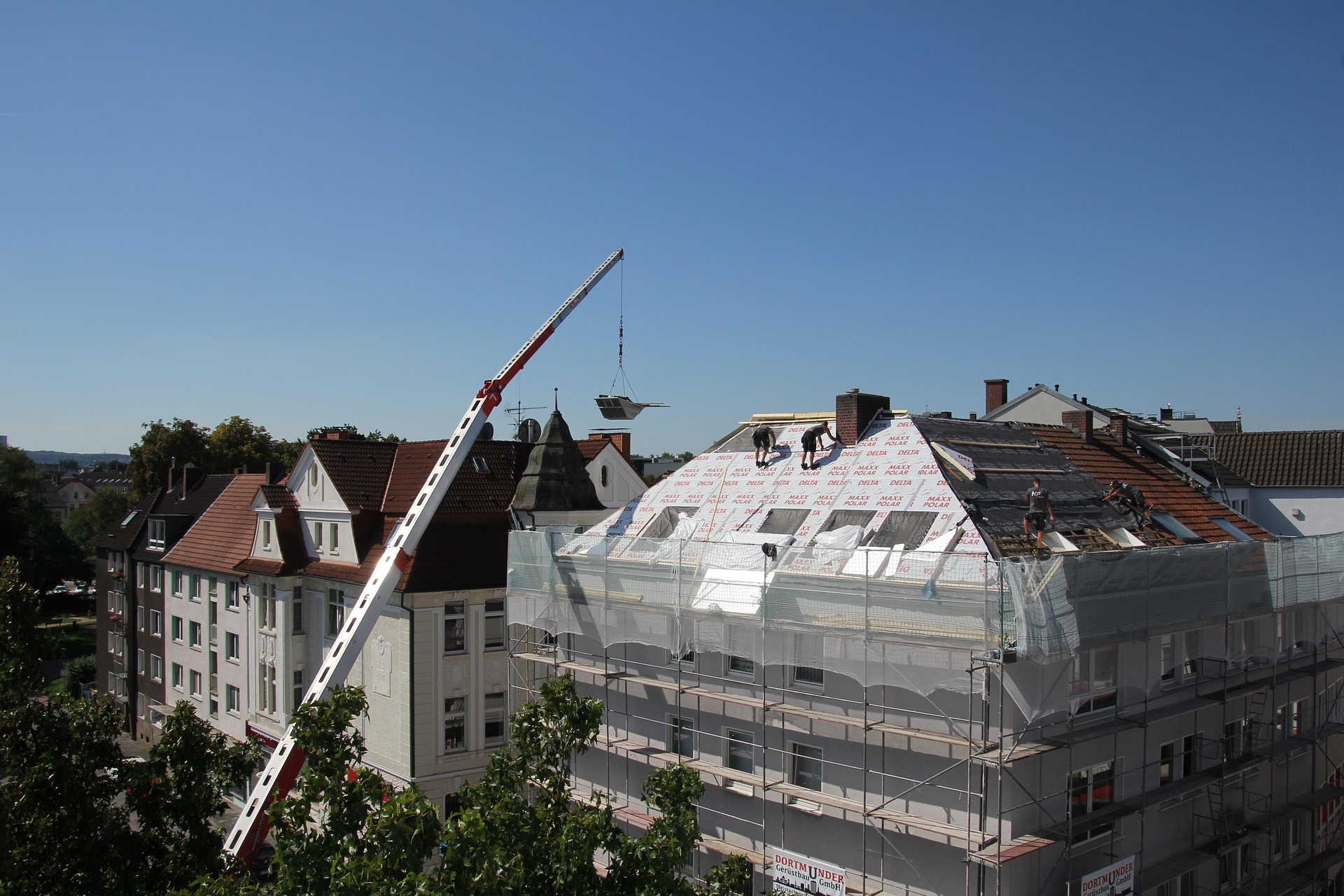 Dachdecker bei der energetischen Sanierung eines Miethauses. Für eine solche Modernisierung wird eine Mieterhöhung in Form einer Modernisierungsumlage fällig.